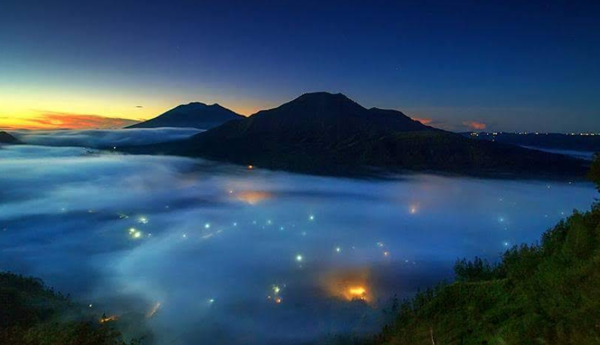 Pemandangan sunset di atas awan dari Desa Pinggan Kintamani dengan latar belakang Gunung Batur dan Gunung Agung yang megah.