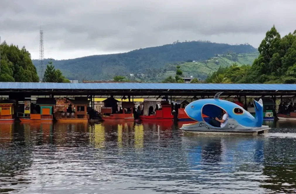 Floating Market Lembang, tampak seorang pria menaiki perahu model ikan. ada perahu yang di dalamnya banyak berjualan makanan