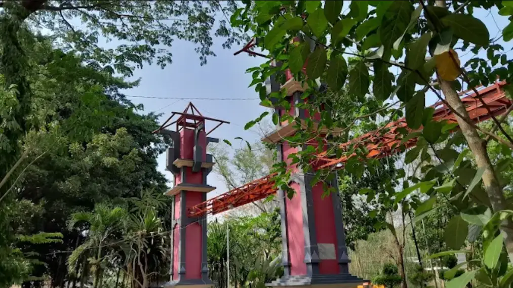 pintu gerbang hutan tinjomoyo. tampak gerbang tugu berwarna merag, dikelilingi pepohonan yang rindang