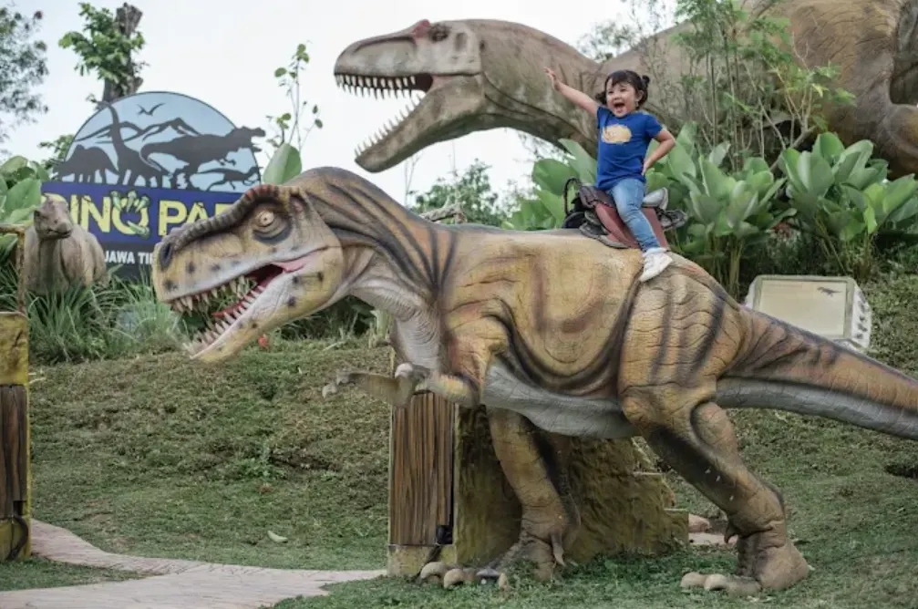 tempat wisata anak jatim park 3. suasananya banyak patung dinosaurus. seorang anak kecil berpose dan berfoto bersama patung dinosaurus