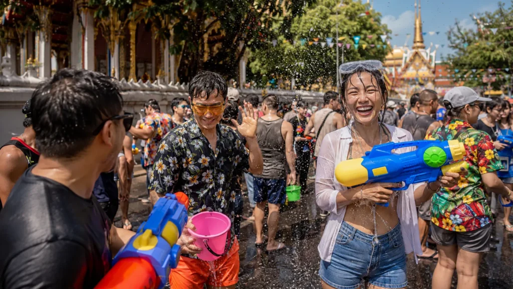 Festival Songkran di Thailand dengan kerumunan warga dan wisatawan bermain air menggunakan pistol air dan ember di depan bangunan kuil.